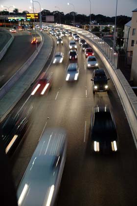 Highway traffic approaching with headlights on at dusk.  A lot happens to keep all this traffic secure from internal and external threats that we never know.  The diminishing light and slight blurring of the headlights hint that transportation  and its security are dynamic systems.  They require continued vigilance to keep up with change.