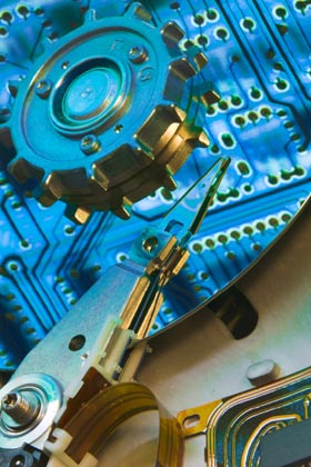 View of the internals of a computer disk drive.  The electronic circuit board is reflected from the mirror-like surface of the disk and mechanical components.  It takes a special skill to pull together complex products composed of software, electronics, and mechanical hardware.